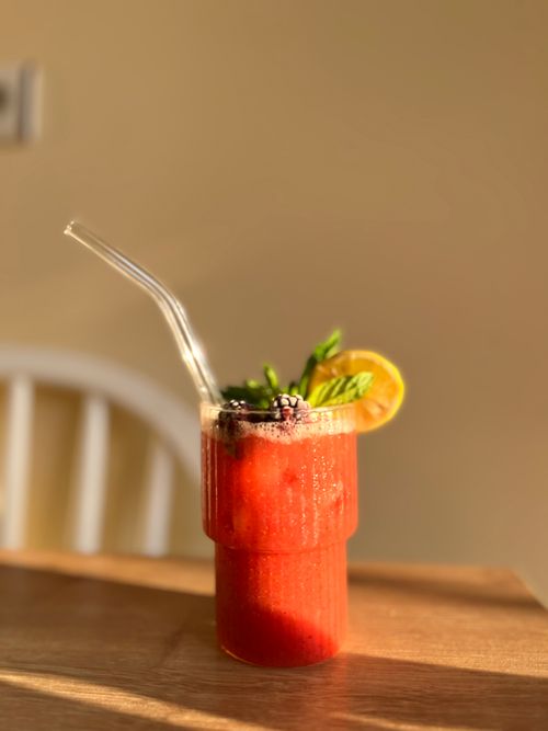 Free A vibrant strawberry lemonade garnished with mint and a lemon slice, captured in warm indoor lighting. Stock Photo