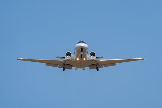 Front view of a private jet approaching for landing against a clear blue sky.