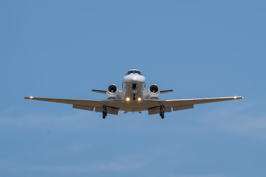 A private jet in flight against a clear blue sky, captured on final approach.