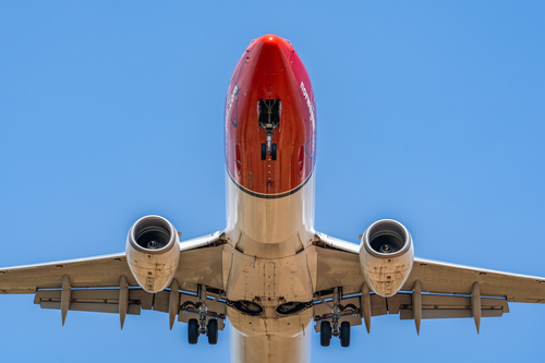 Free A red-nosed commercial airplane in flight captured from below, showcasing landing gear and engines. Stock Photo