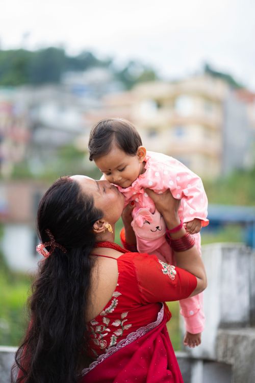 Free A mother lovingly kisses her baby while holding them outdoors, both in colorful attire. Stock Photo