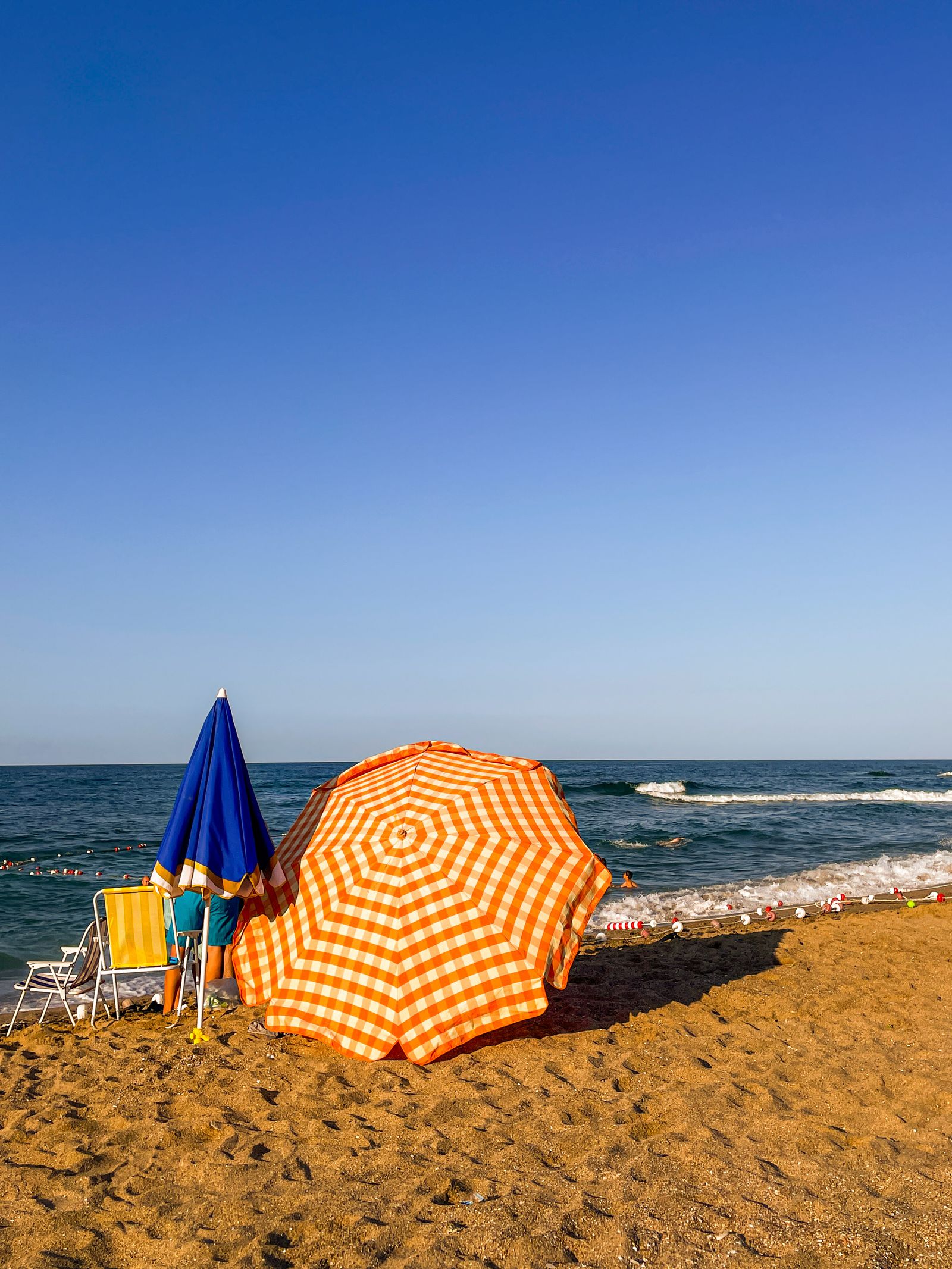 Orange and blue vented beach umbrellas anchored in the sand on a sunny shoreline