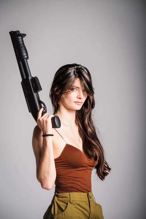 Free A strong and confident woman poses with a shotgun against a neutral studio background. Stock Photo