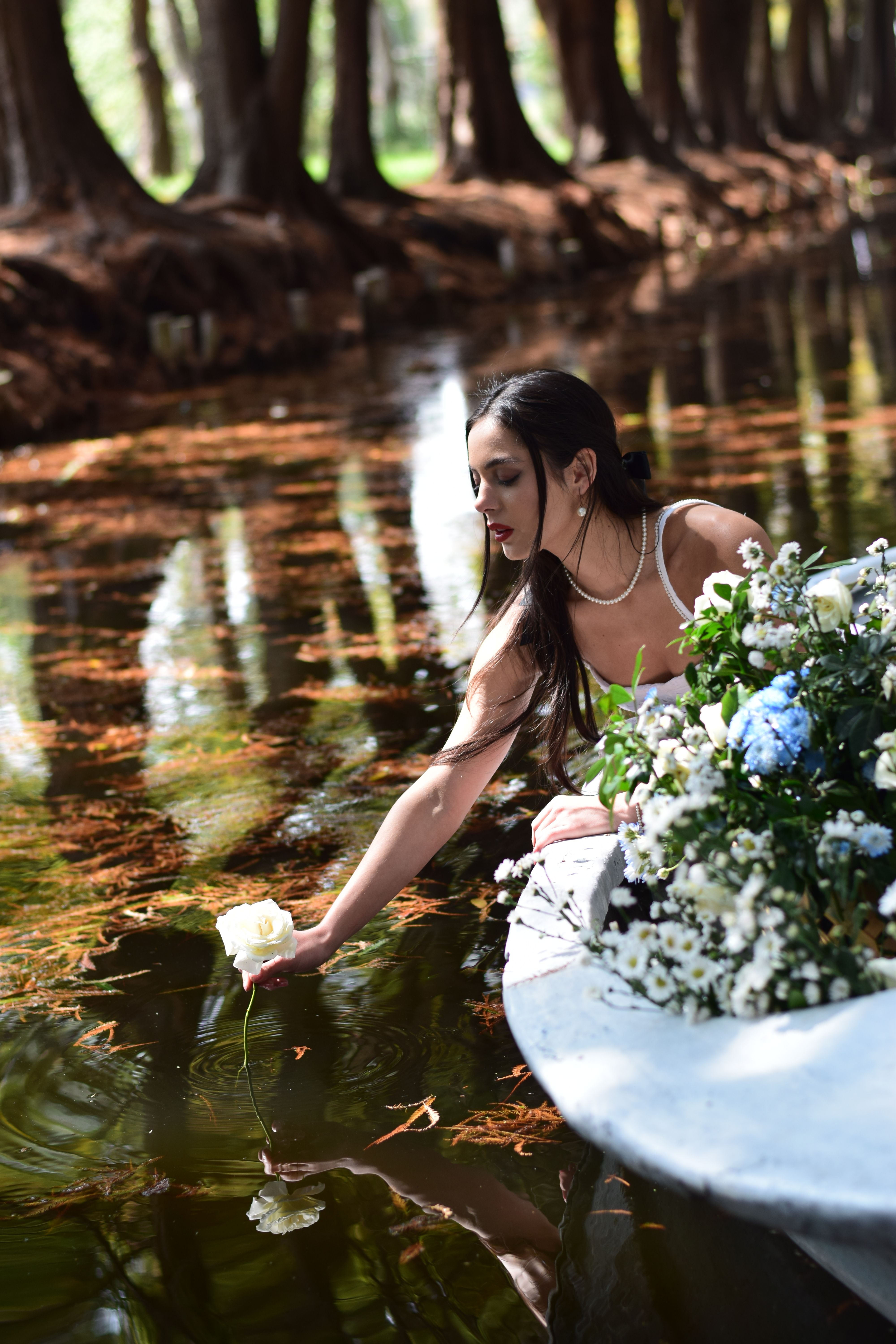 Fotomural Una mujer joven en una canoa alcanza una flor en un río sereno en un bosque.