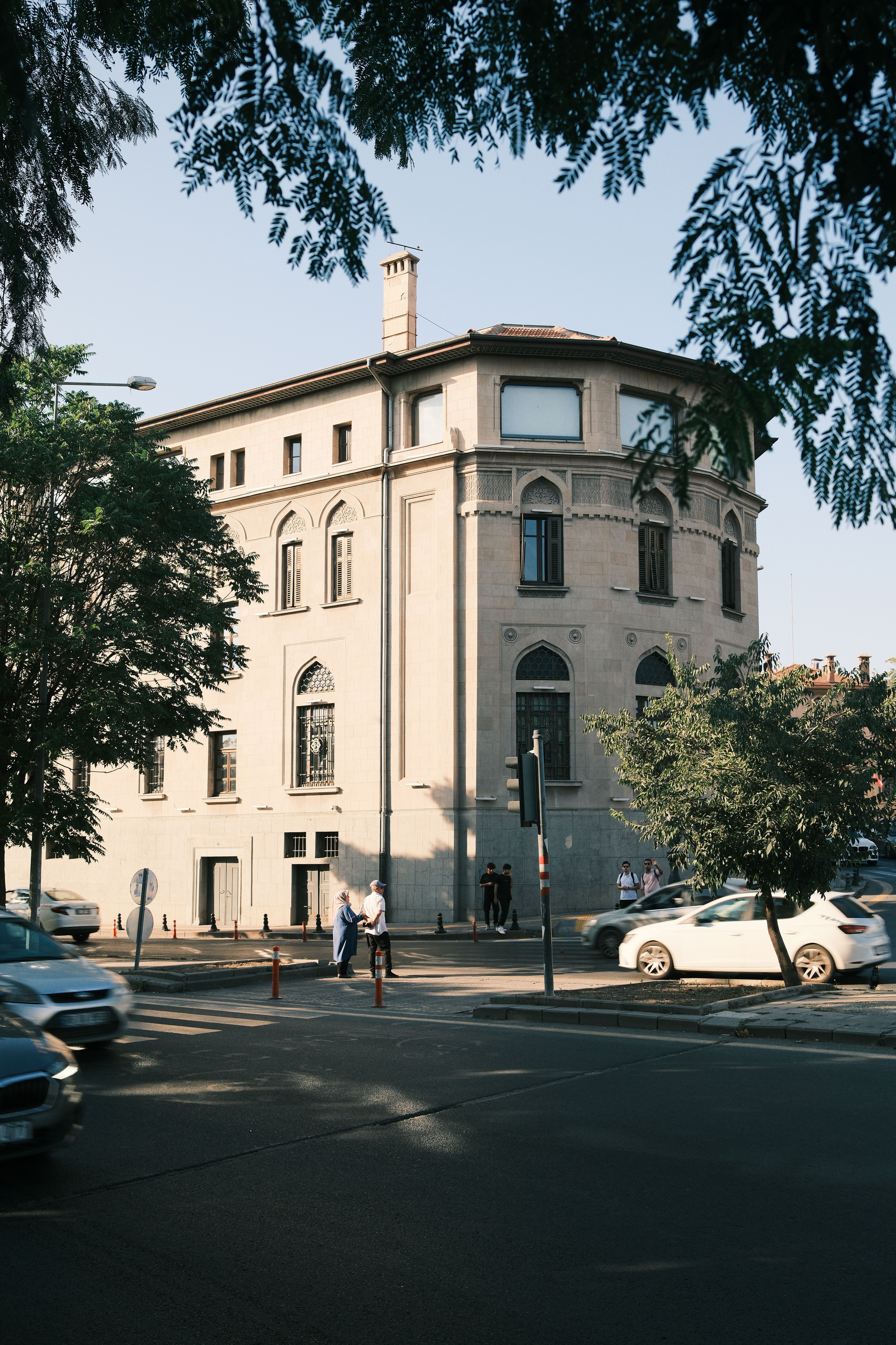 Elegant historic building on bustling street corner with cars and pedestrians.