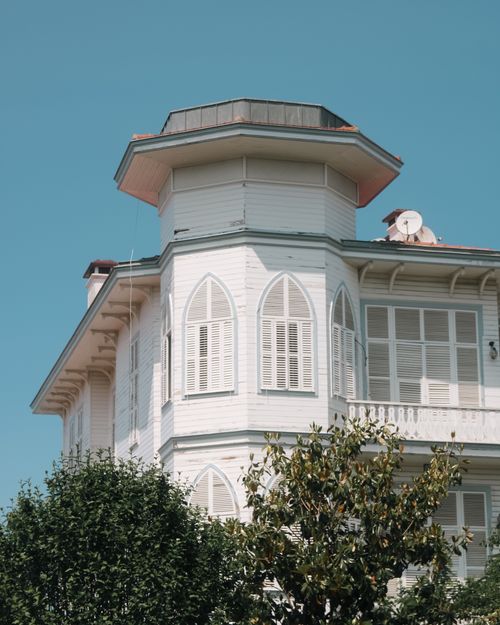 Free A picturesque Victorian-style house with distinct shutters under a clear blue sky, surrounded by lush greenery. Stock Photo