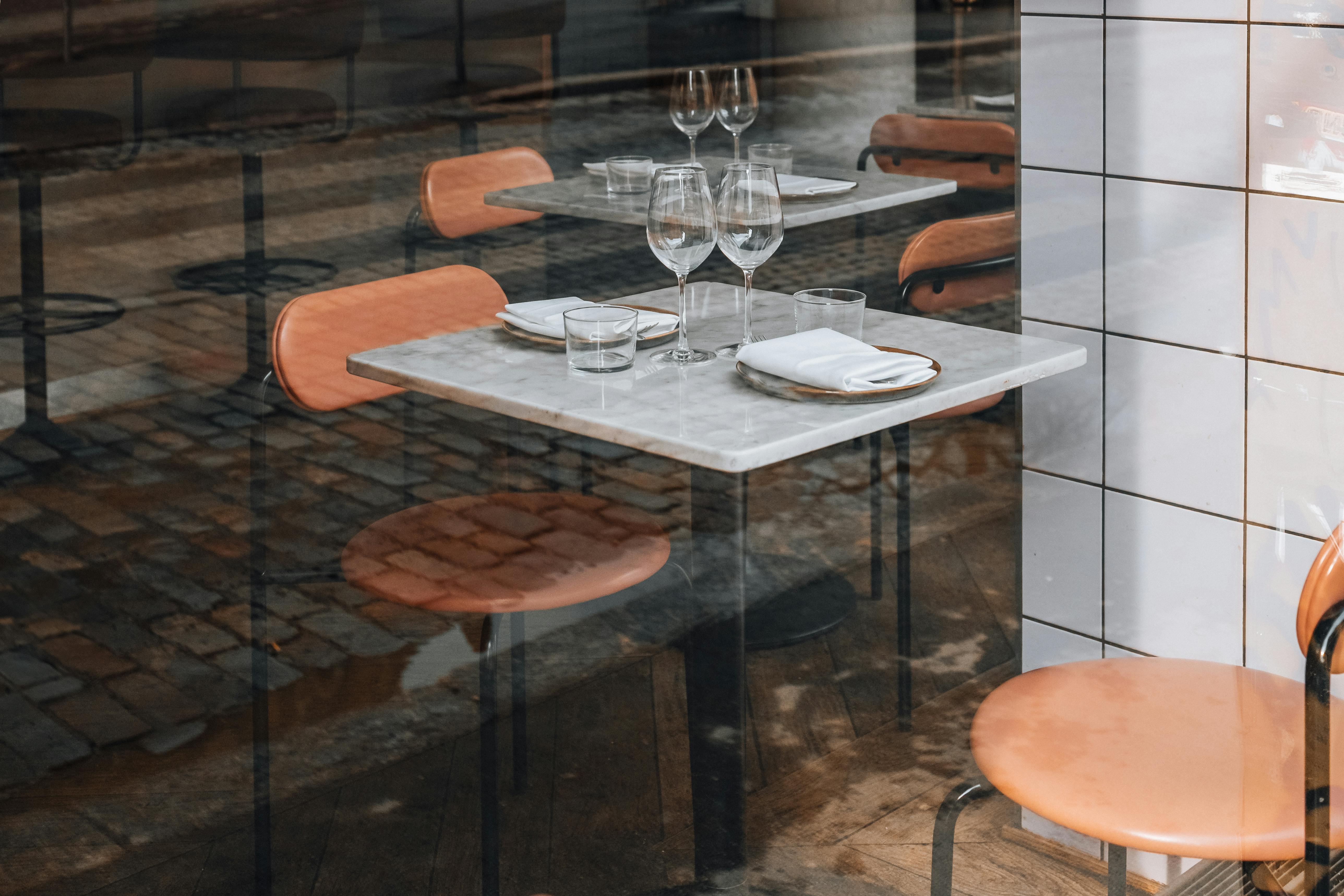 A cozy cafe table setup with wine glasses and napkins, reflecting urban street view.