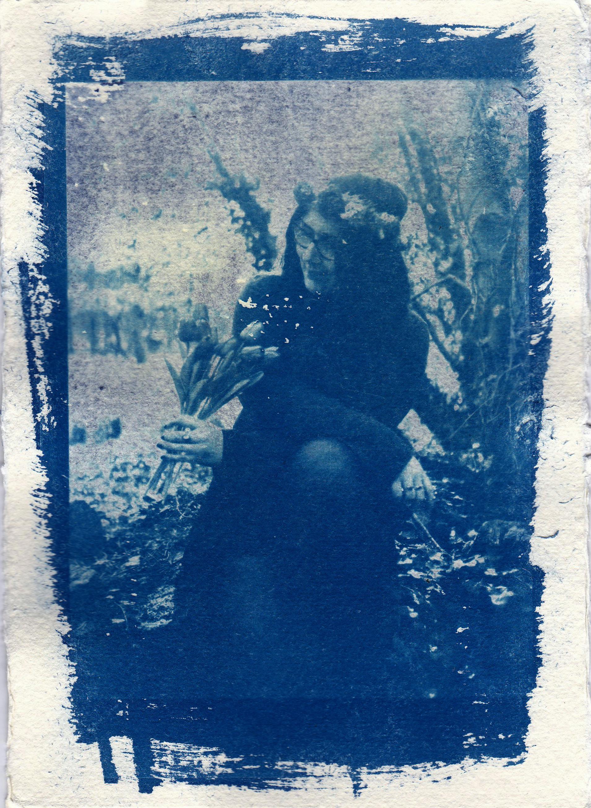 Artistic cyanotype of woman outdoors, holding flowers in timeless vintage style.
