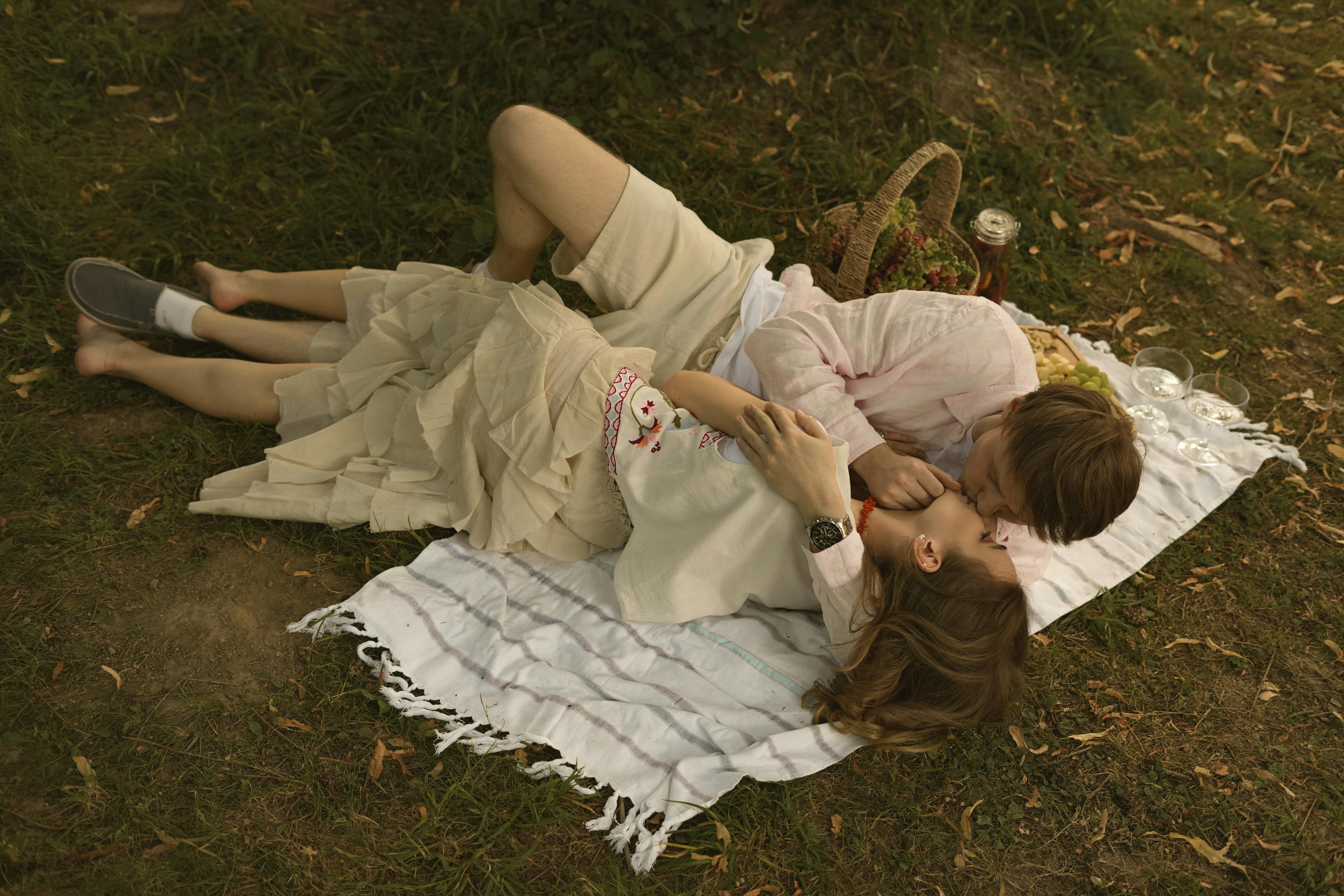A couple enjoying a romantic picnic outdoors, lying on a blanket and sharing an intimate moment.