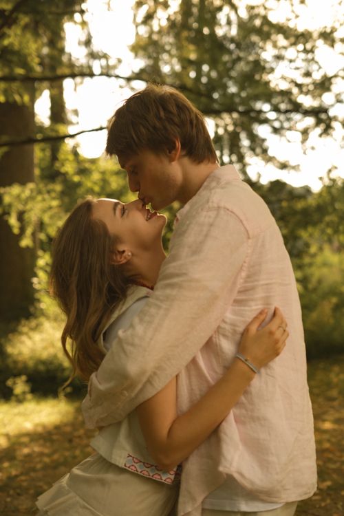 Free A couple shares a loving embrace in a sunlit park, surrounded by lush greenery. Stock Photo