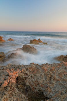 Captivating long exposure shot of rocks and waves at sunset, creating an ethereal seascape.