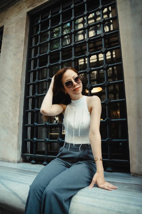 Free Chic young woman in sunglasses poses by a decorative window, exuding confidence and style. Stock Photo
