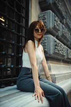 Elegant woman with sunglasses relaxing on a stone ledge outdoors. Urban fashion vibe.