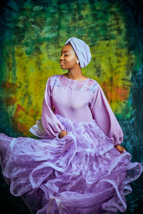 Free Elegant woman in a lavender dress poses gracefully against a vibrant abstract backdrop. Stock Photo