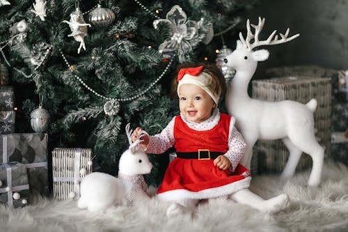 Free Baby Girl Wearing Santa Dress Sitting Beside Christmas Tree Stock Photo