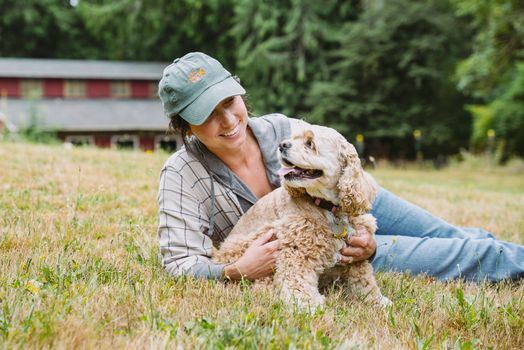 Young woman lying on grass with Cocker Spaniel dog on a sunny day in a rural setting.