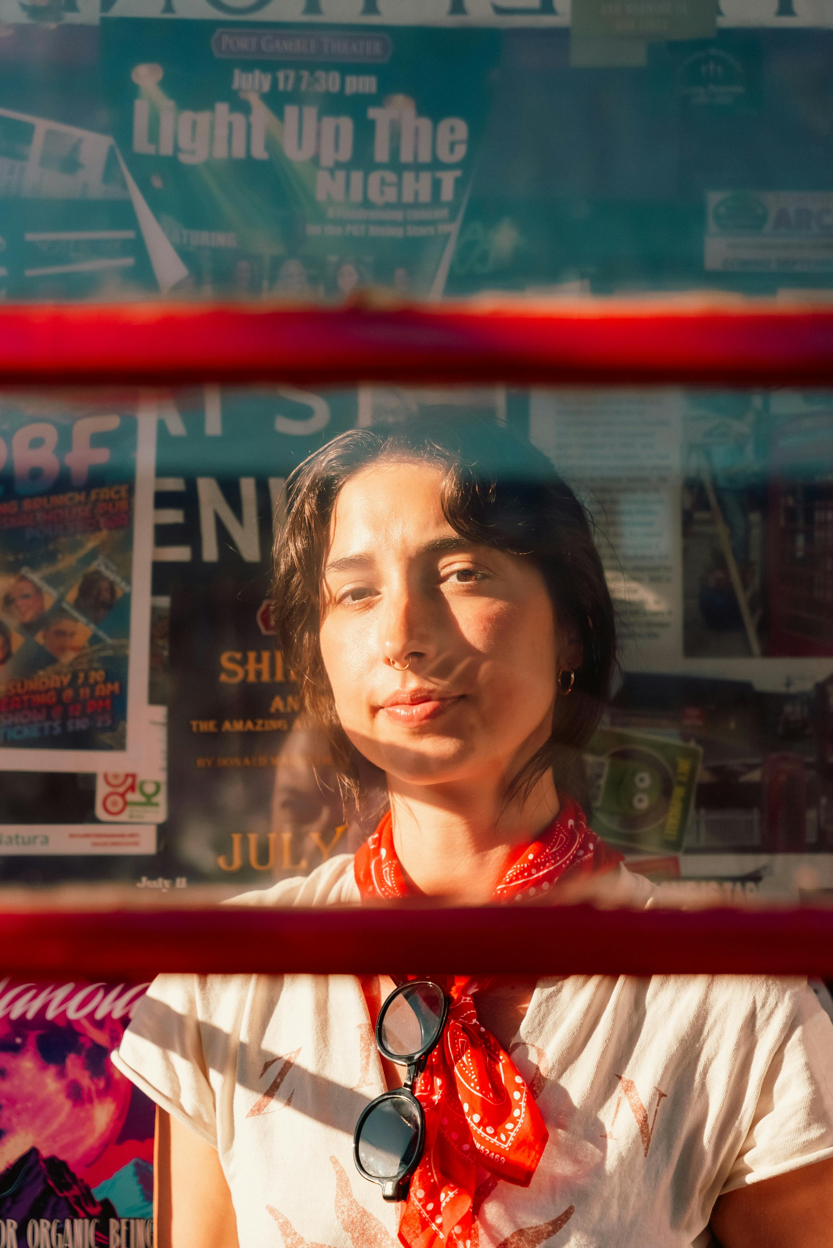 Outdoor portrait of a woman wearing a red scarf viewed through glass, capturing summer sunlight.