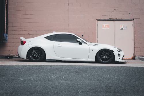 Free A stylish white sports car parked against a brick wall, showcasing its sleek design. Stock Photo