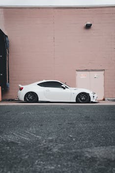 A stylish white sports car parked beside a pink brick wall in an urban setting.