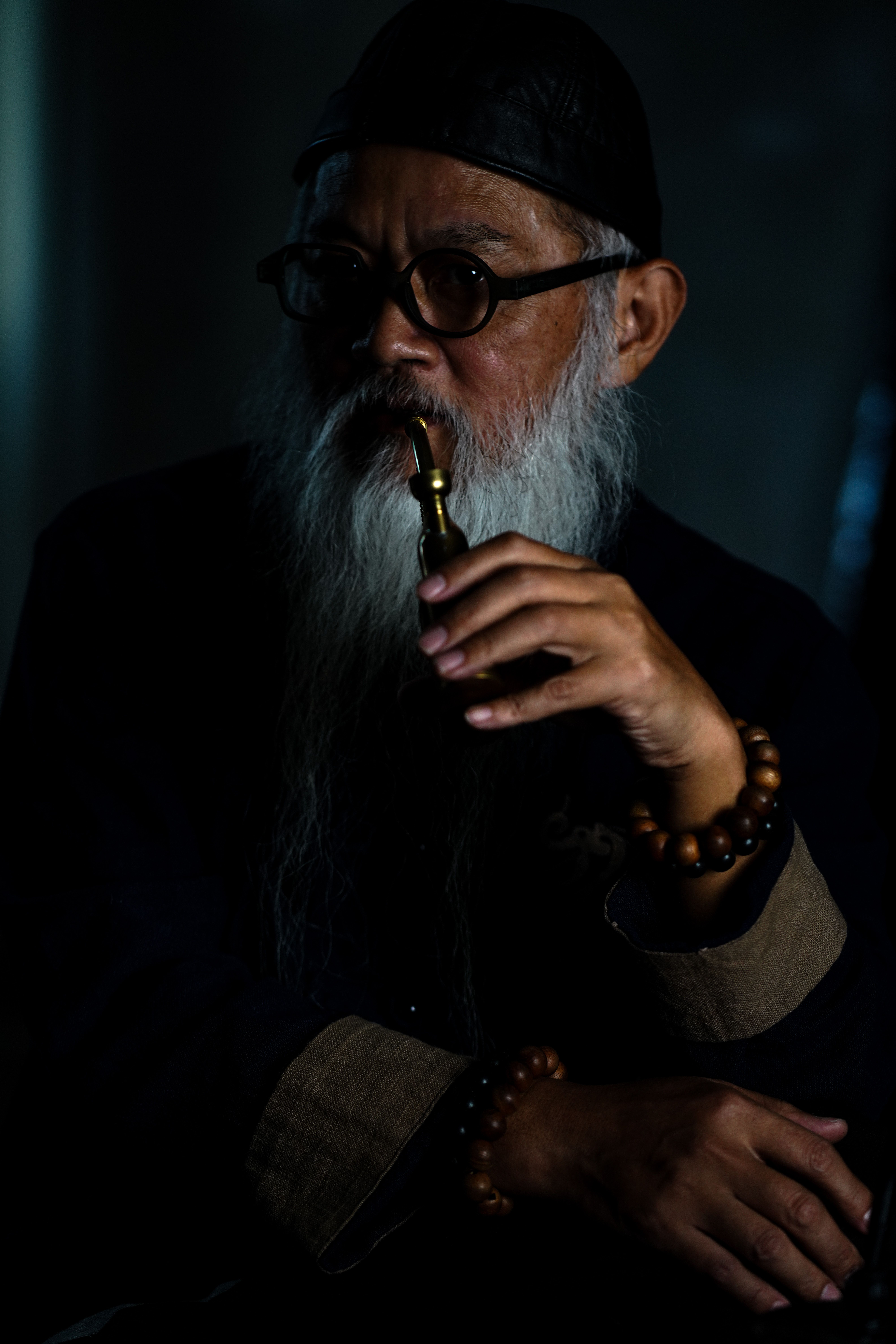 Elderly man with glasses and beard in thoughtful pose indoors, Bandung