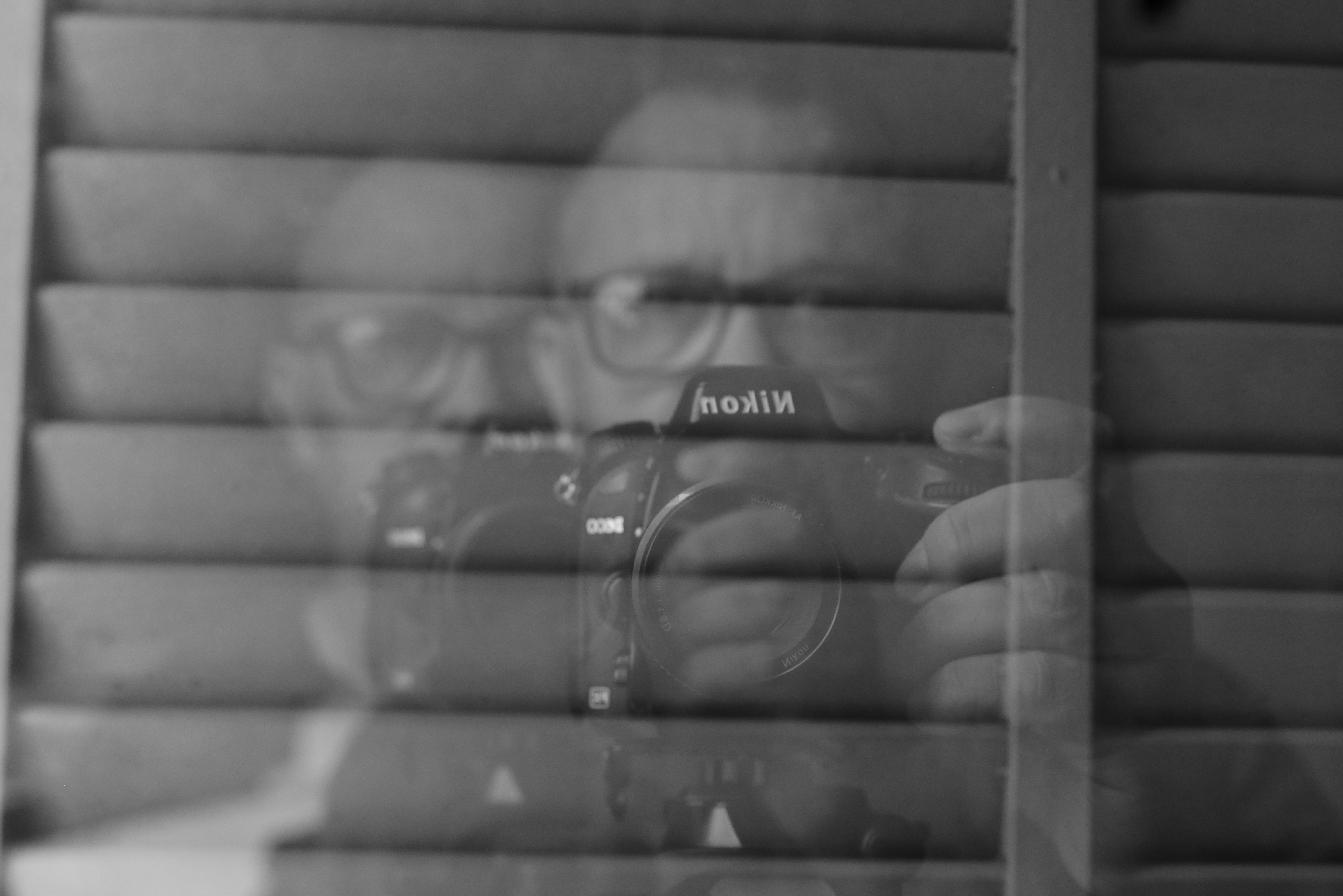 Creative black and white reflection self-portrait of a person holding a camera, artistic composition.