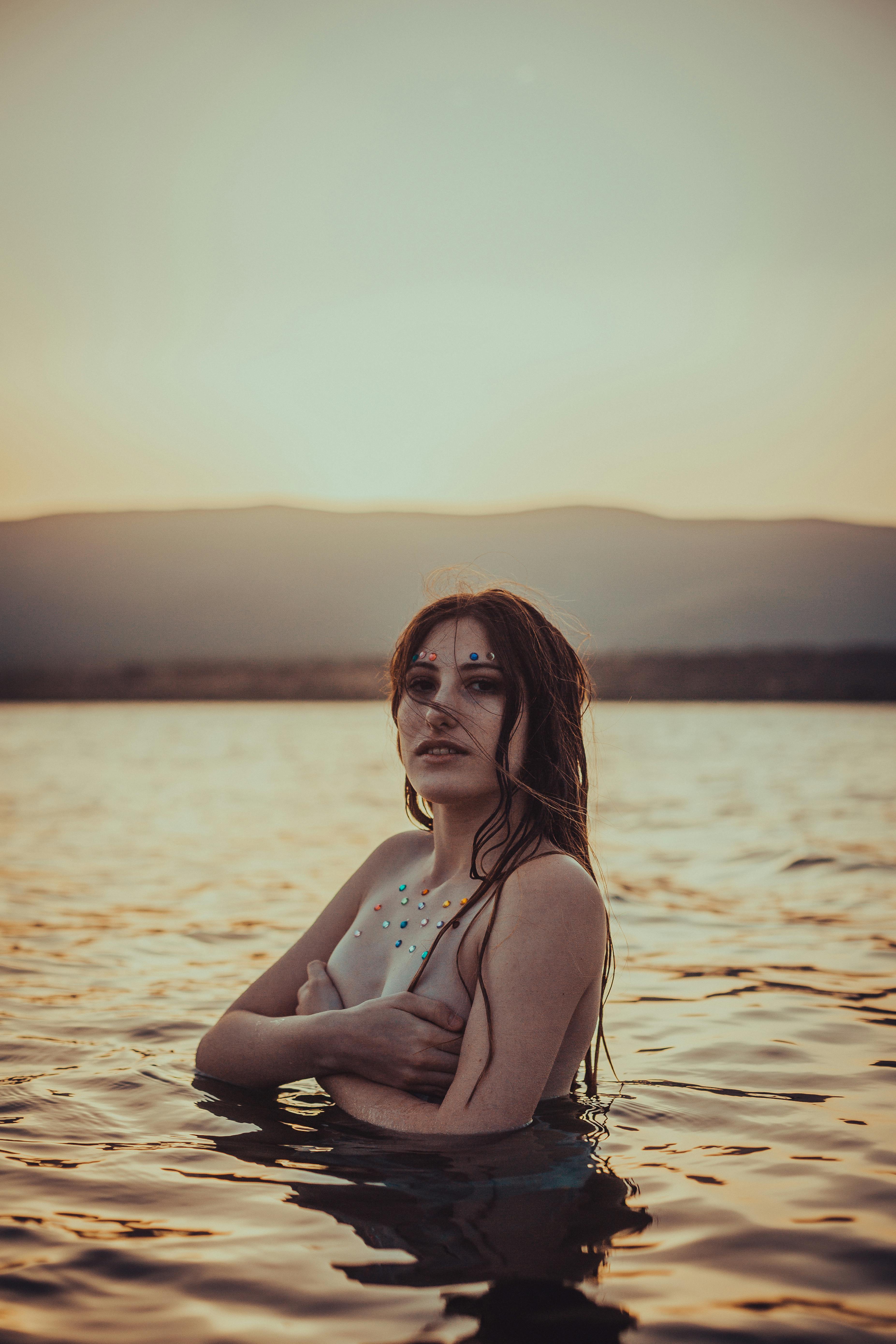 topless woman on body of water during sunset