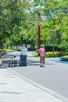 Two senior adults walking in a sunlit, green park enjoying leisure time and nature.