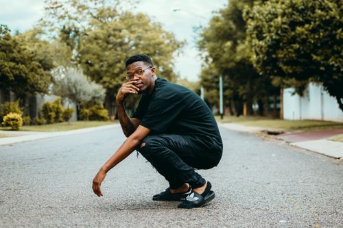 Free Young man squatting on a city street in a thoughtful pose. Stock Photo