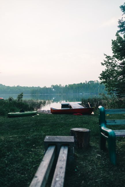 A calm lake at sunrise with a canoe pulled up on a rocky shoreline in La Mauricie National Park