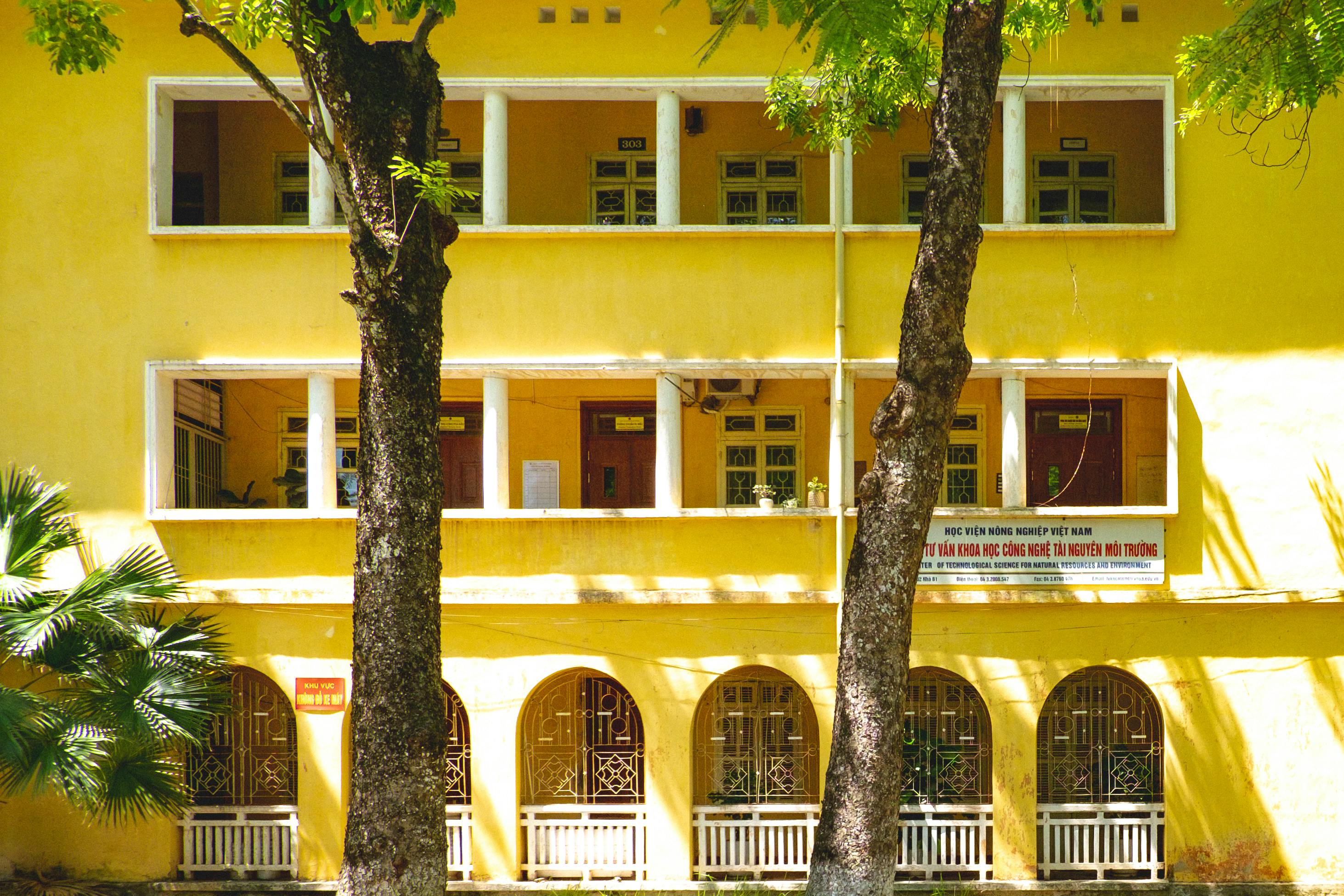 Yellow colonial-style university building surrounded by lush greenery in Hanoi, Vietnam.