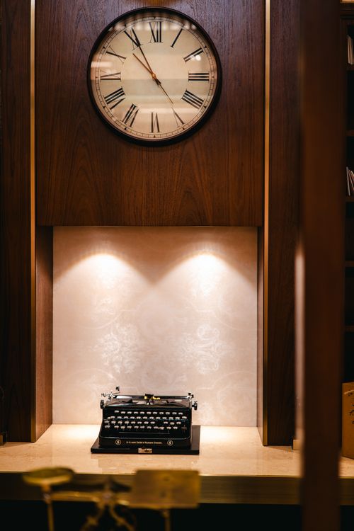 Free A vintage typewriter displayed beneath a classic wall clock in a warm, elegant setting. Stock Photo