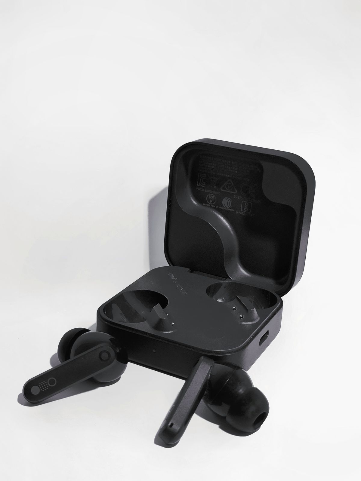 Black wireless earbuds resting in an open charging case on a white background, ready for cleaning