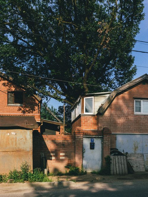 Free A suburban scene featuring a brick house overshadowed by a large tree, capturing a tranquil residential atmosphere. Stock Photo