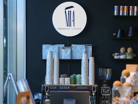 A stylish coffee shop interior featuring premium coffee branding, stacks of cups, and coffee brewing equipment.