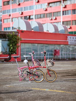 Two vibrant folding bikes in an urban setting with a striking pink building in the background.