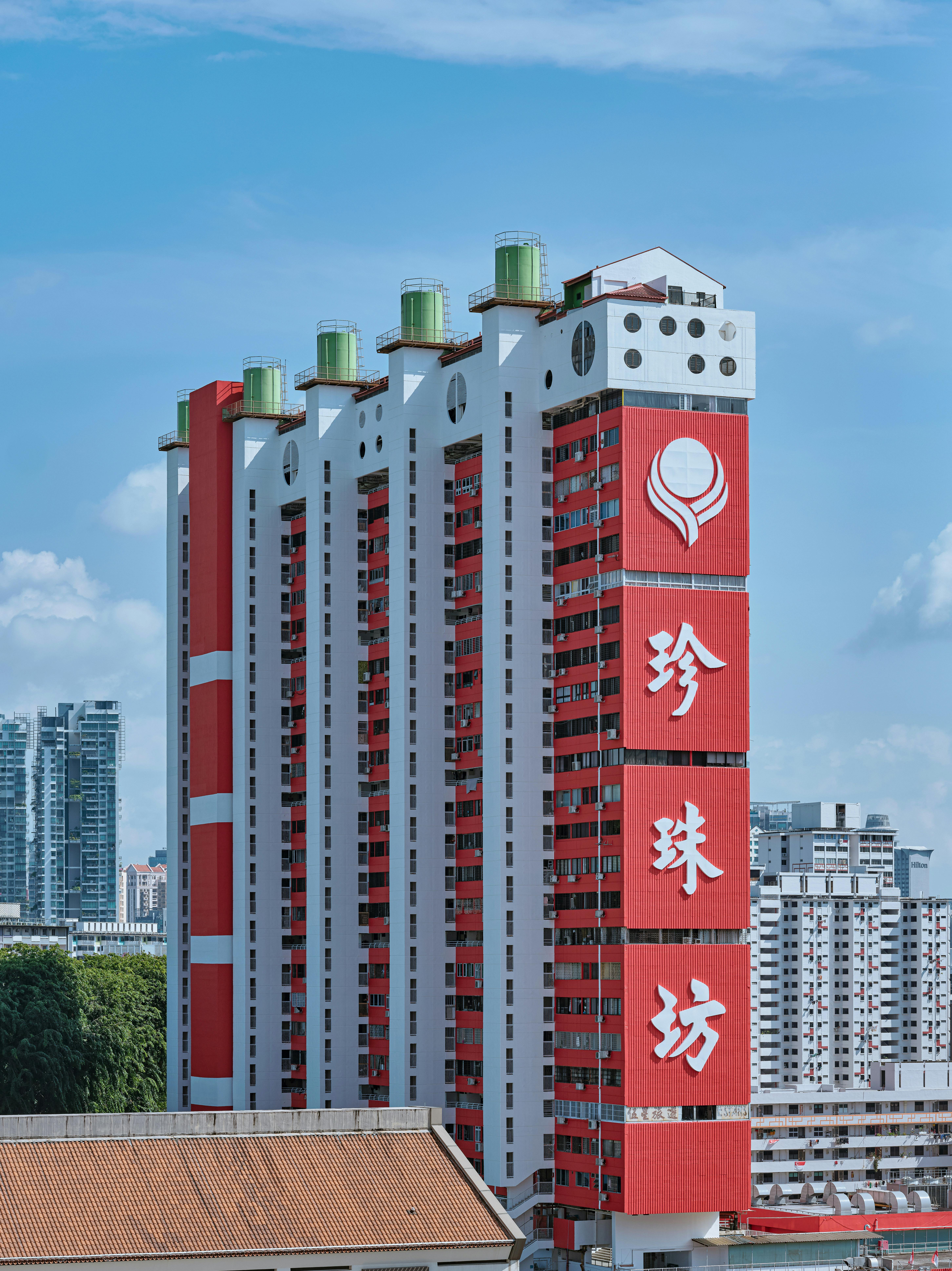 Vertical red and white residential building with signage against a clear blue sky in Singapore.