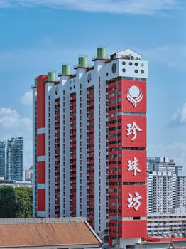 Vertical red and white residential building with signage against a clear blue sky in Singapore.