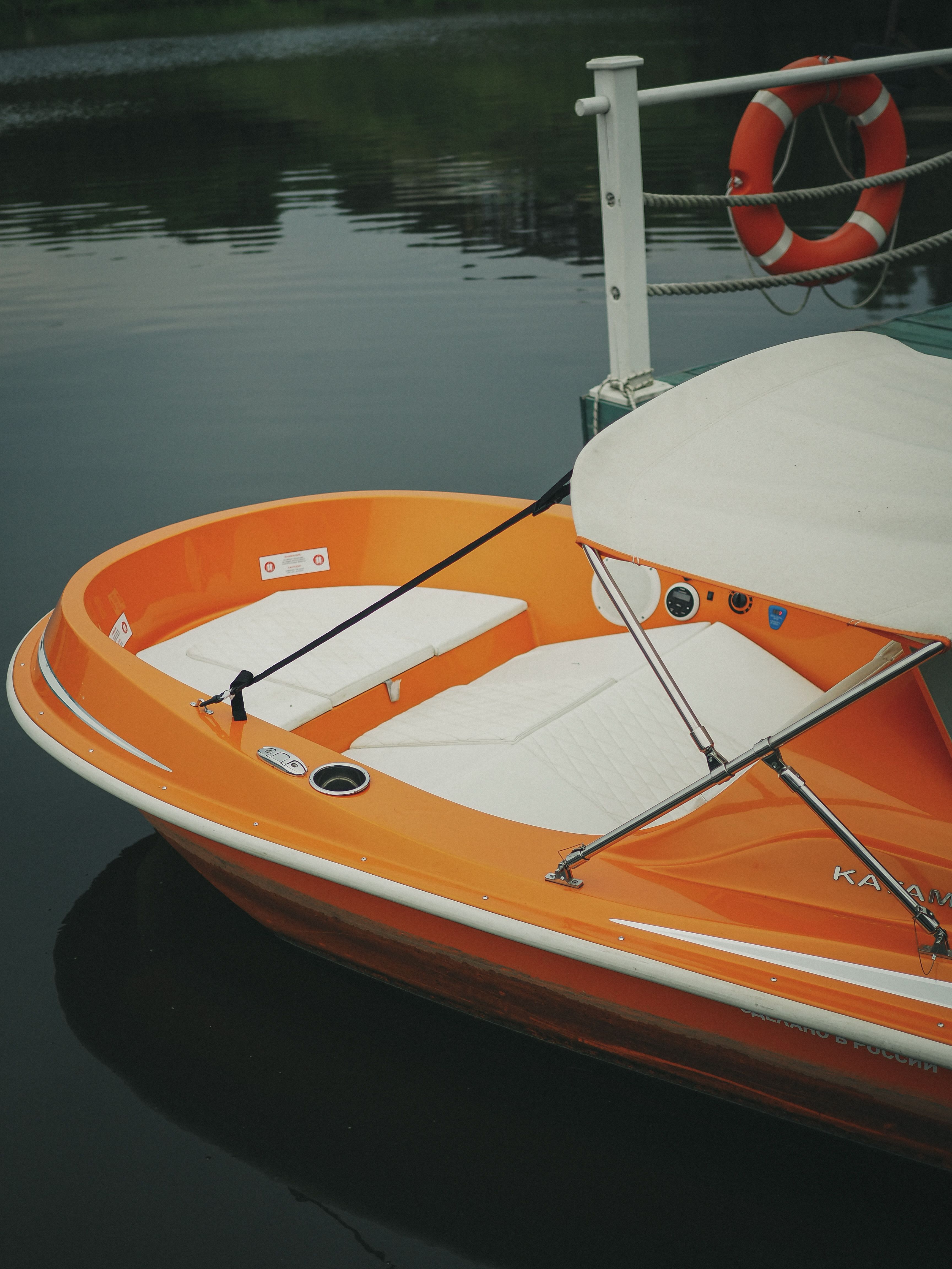A vibrant orange paddle boat secured to a dock over calm waters with a life preserver nearby.