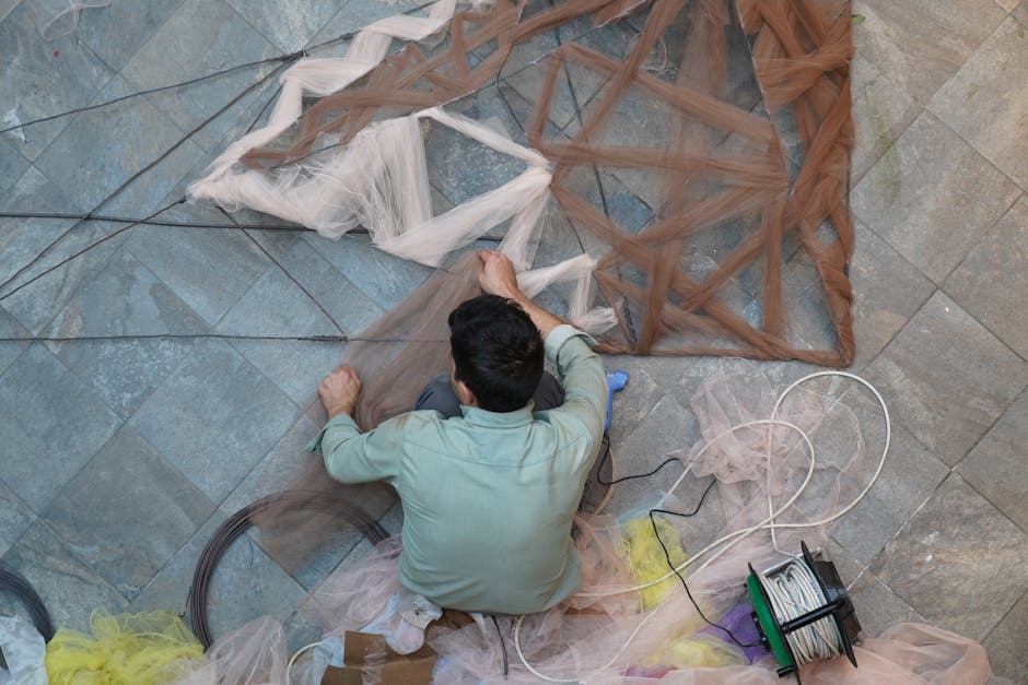 A person skillfully crafting a large mesh structure indoors using wire and fabric.