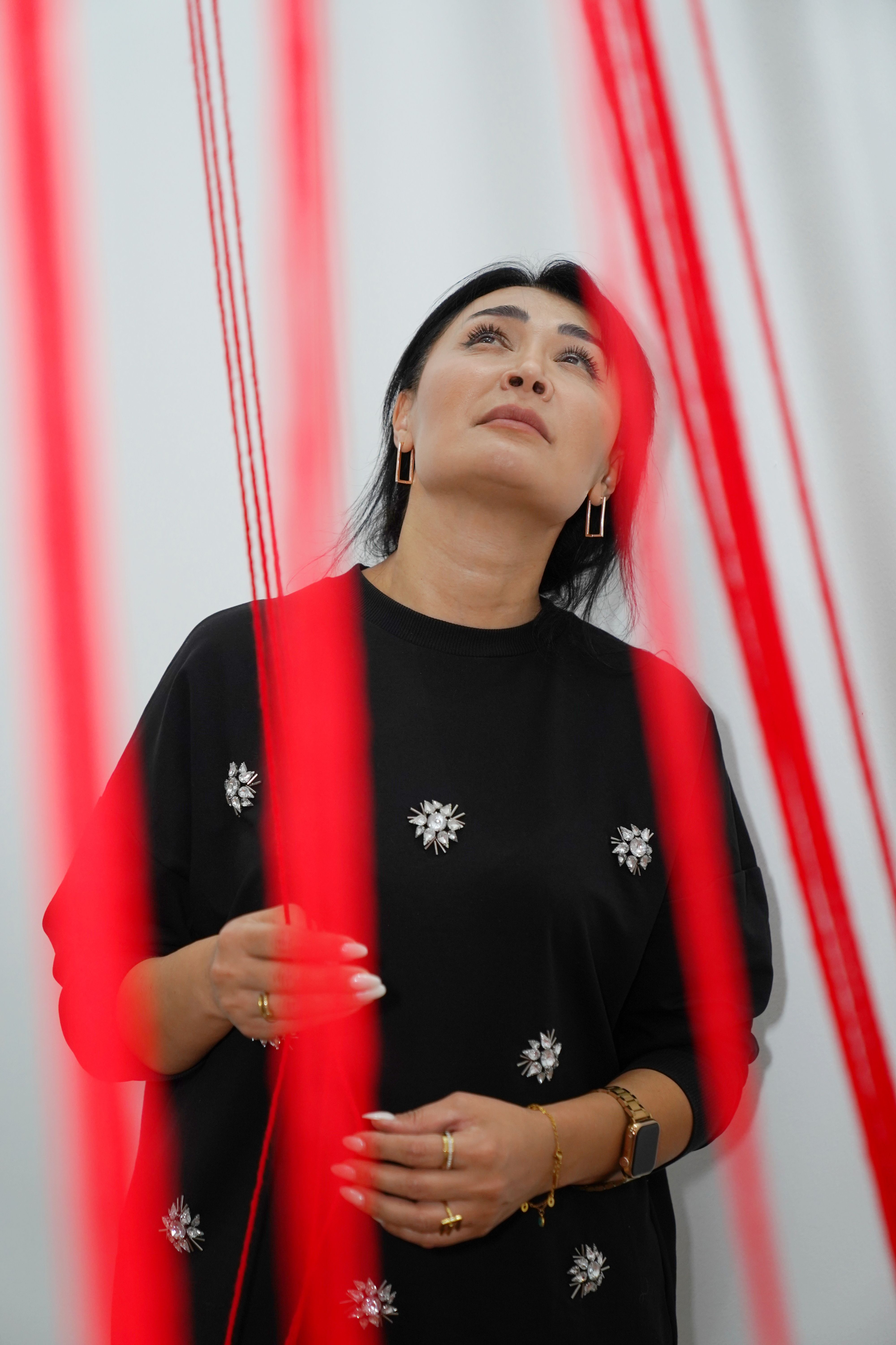 A woman stands among red strings, gazing upwards, in a modern art installation.
