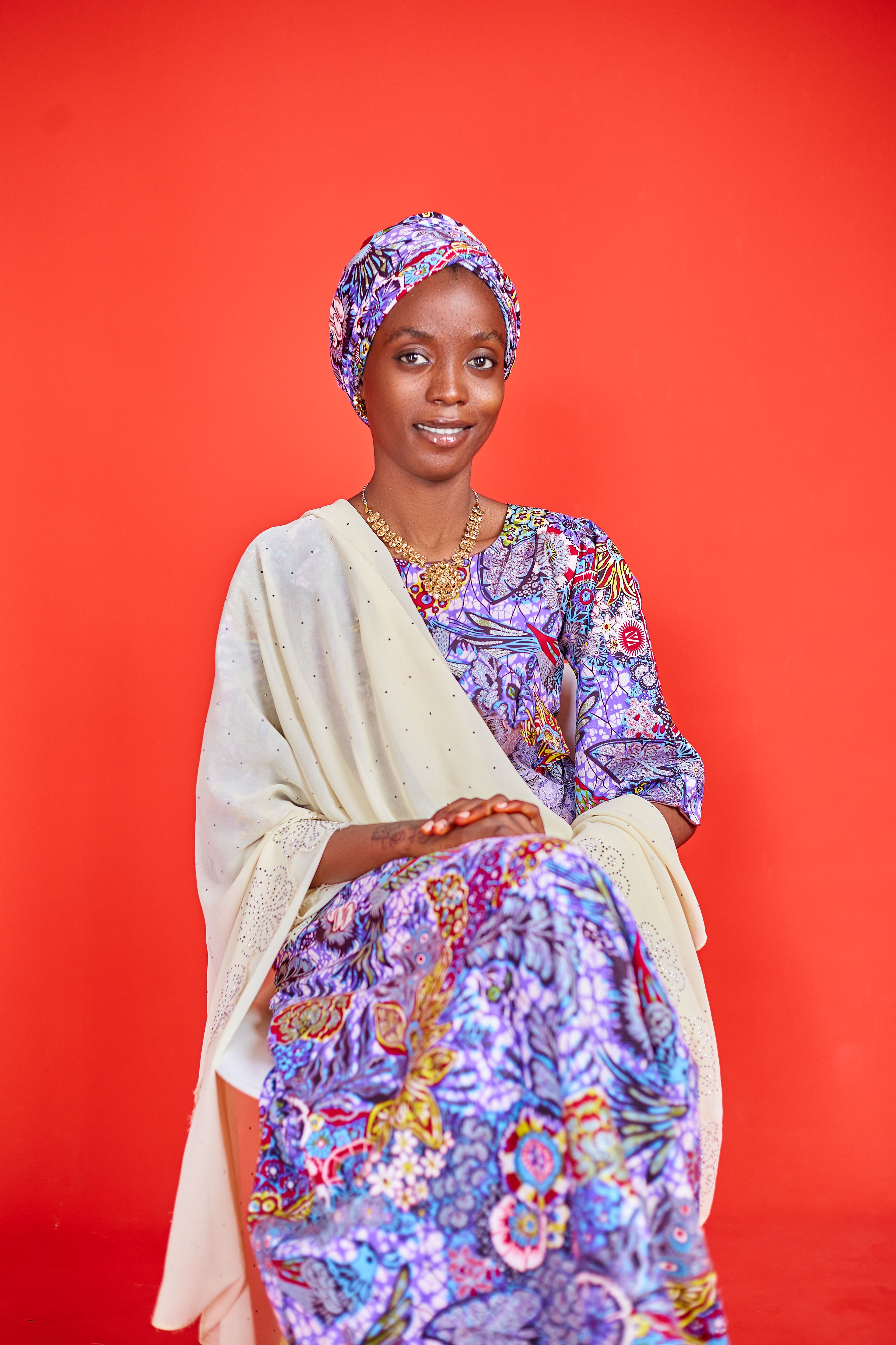 Woman in colorful traditional dress against vibrant red background, smiling.