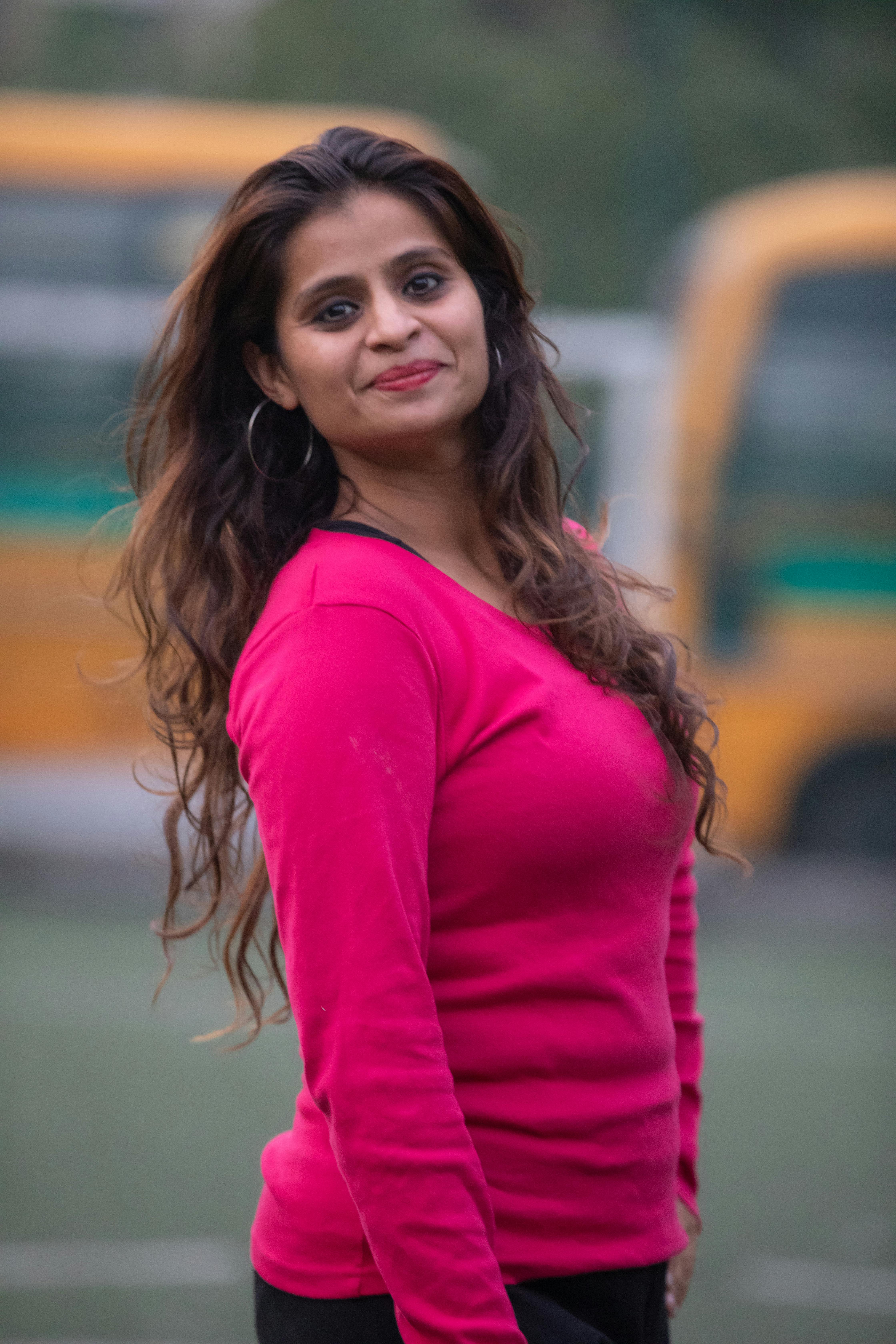 Smiling young woman in pink sweater outdoors with blurred yellow buses in background.