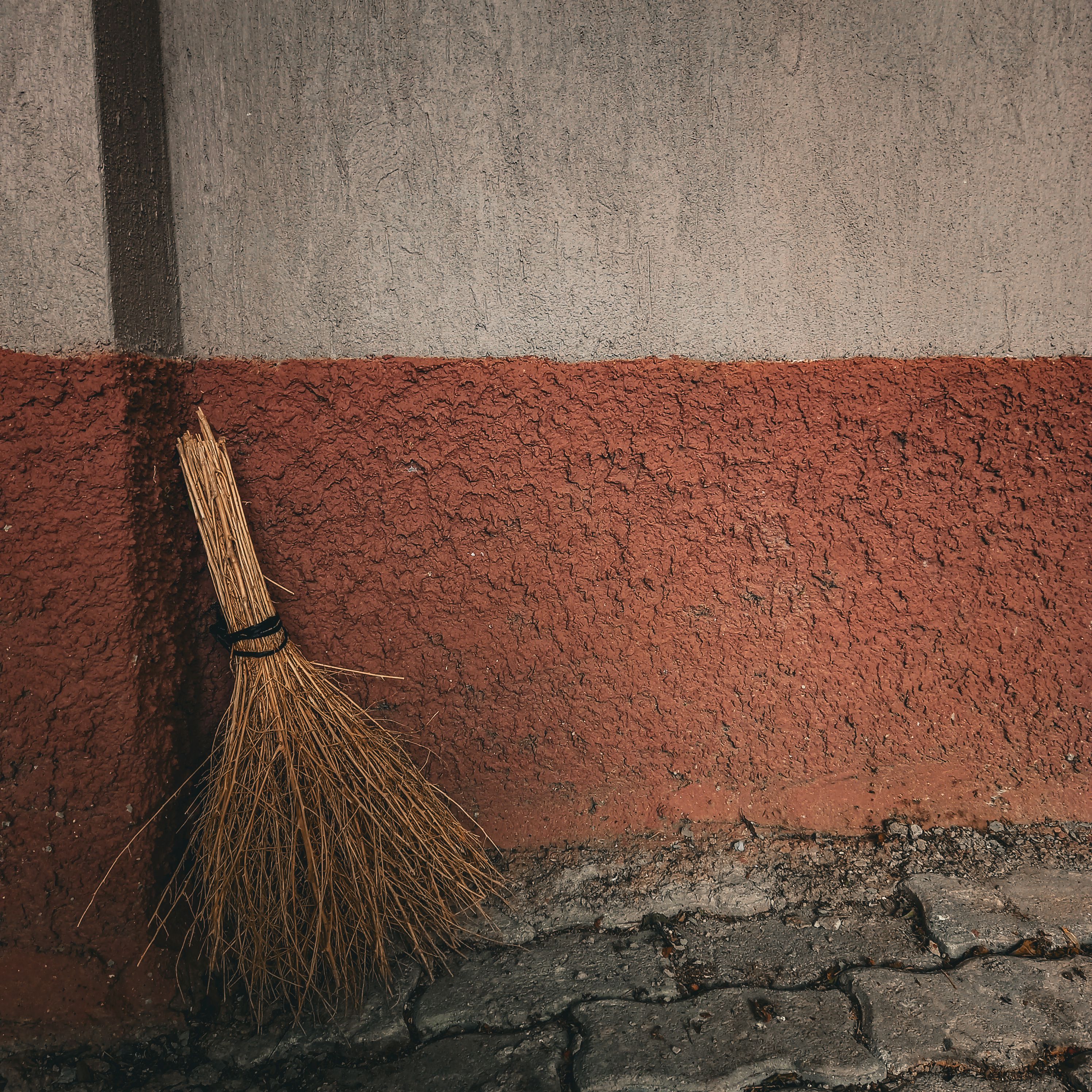 A rustic broom leans against a textured wall, showcasing simple, traditional tools.