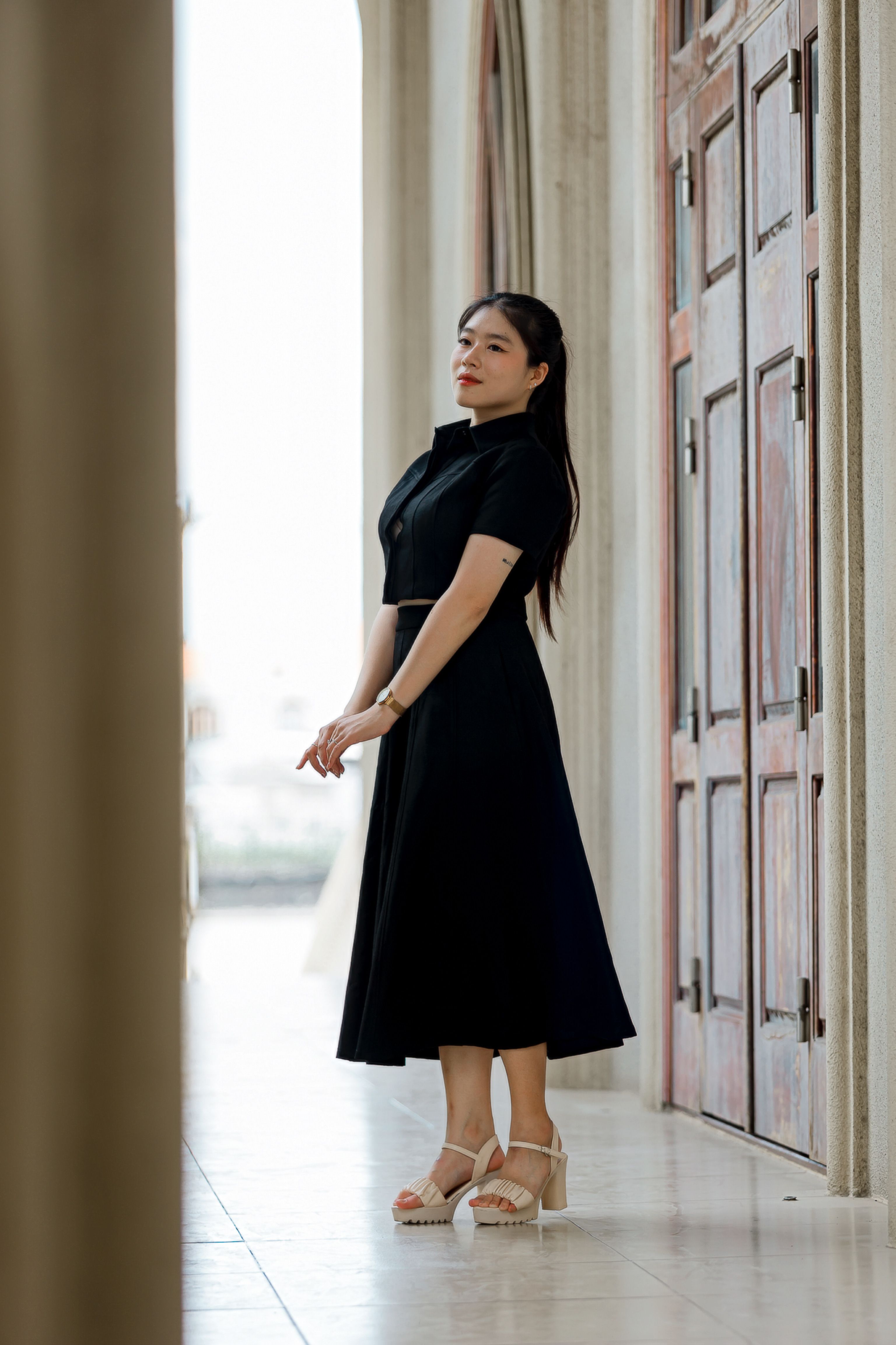 Elegant Woman in Black Dress in Sunlit Corridor · Free Stock Photo