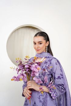 Fashion model in a purple eastern dress holding flowers in a Lahore studio.