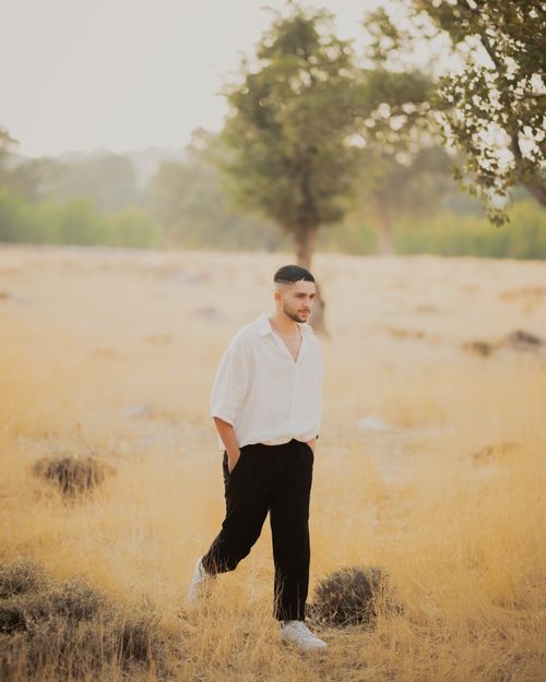 Free Young male model in casual attire walking through a sunny field, captured in warm natural light. Stock Photo