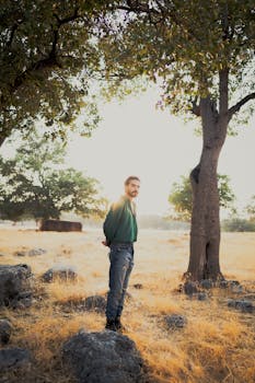 A portrait of a man standing in a sunlit field with trees, captured during golden hour.