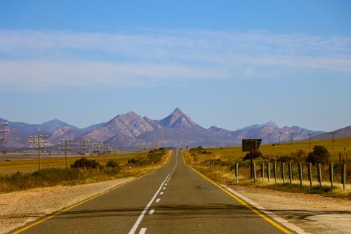 Free Wide open road leading to stunning mountain range under clear blue sky. Stock Photo
