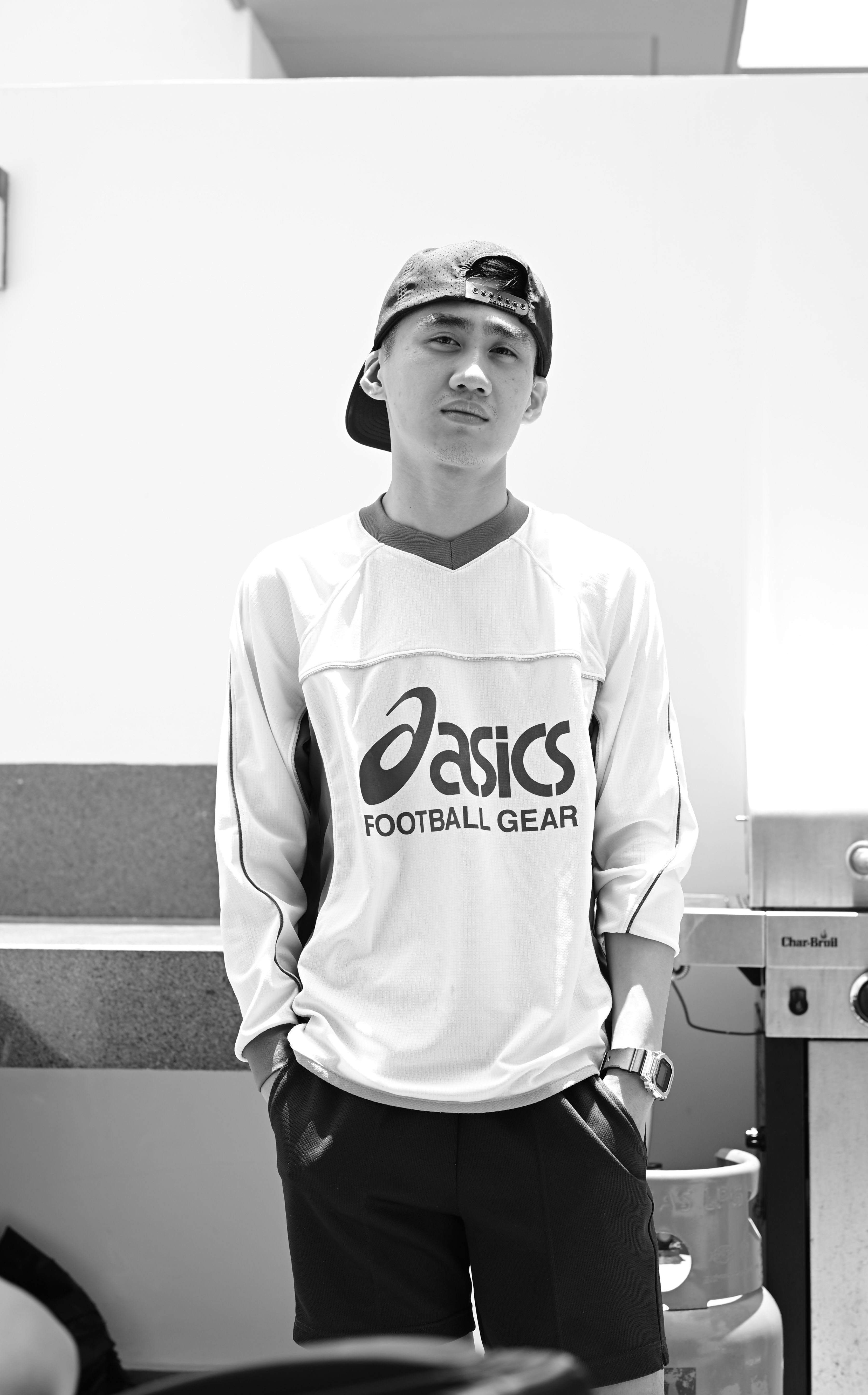 Black and white portrait of a young adult wearing casual clothing and a cap outdoors.