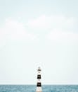 一座孤独的灯塔矗立在晴朗的天空和平静的海洋的映衬下，展现了极简主义的宁静